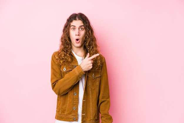 Hombre joven de pelo largo posando aislado apuntando hacia el lado