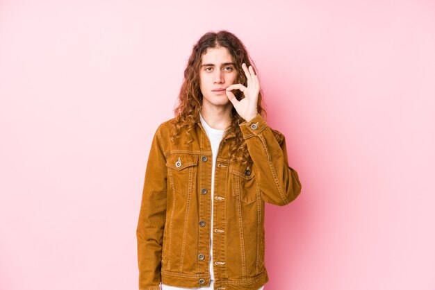 Hombre joven de pelo largo posando aislado con los dedos en los labios guardando un secreto.