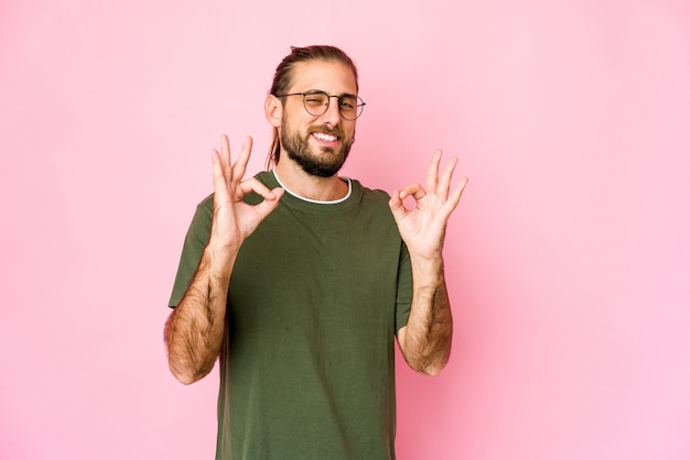 El hombre joven con el pelo largo se ve alegre y confiado mostrando un gesto bien.