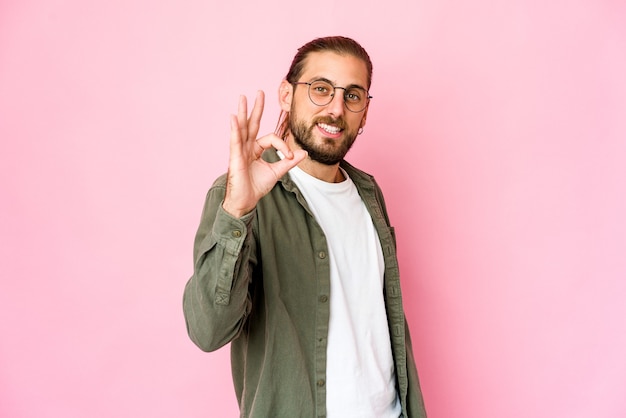 El hombre joven con el pelo largo se ve alegre y confiado mostrando un gesto bien.