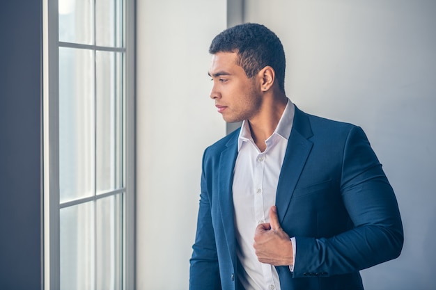 Hombre joven de pelo oscuro en elegante traje mirando pensativo