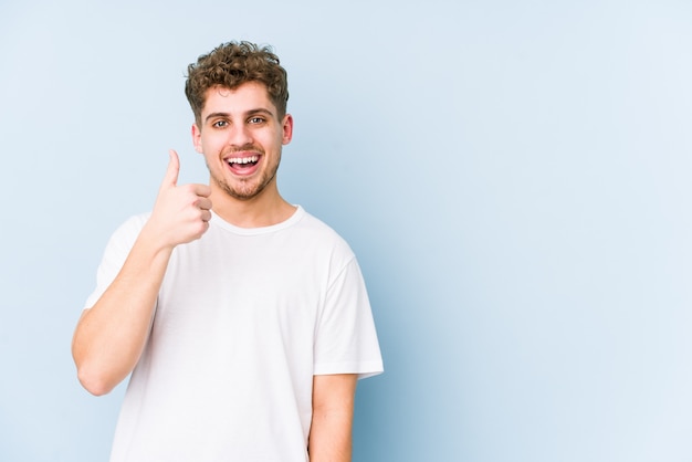 Hombre joven de pelo rizado rubio sonriendo y levantando el pulgar hacia arriba