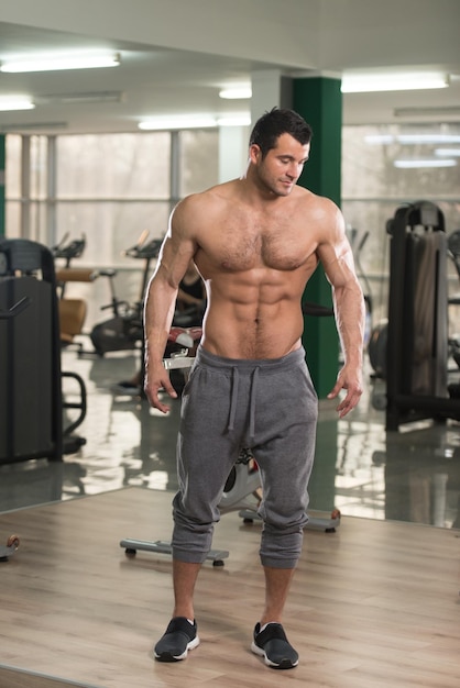 Hombre joven peludo y saludable de pie fuerte en el gimnasio y flexionando los músculos Muscular culturista atlético modelo de fitness posando después de los ejercicios