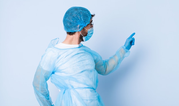 Hombre joven de pie y apuntando al objeto en el espacio de la copia, vista trasera. concepto de coronavirus