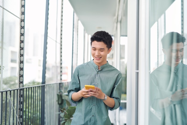 Hombre joven de pie en el balcón enviando mensajes de texto por teléfono móvil,