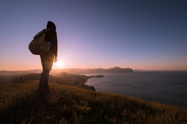 Hombre joven de pie con mochila. Caminante en la piedra en la orilla del mar en el colorido cielo del atardecer. Hermoso paisaje con hombre deportivo rocas mar y nubes al atardecer. Estilo de vida deportivo