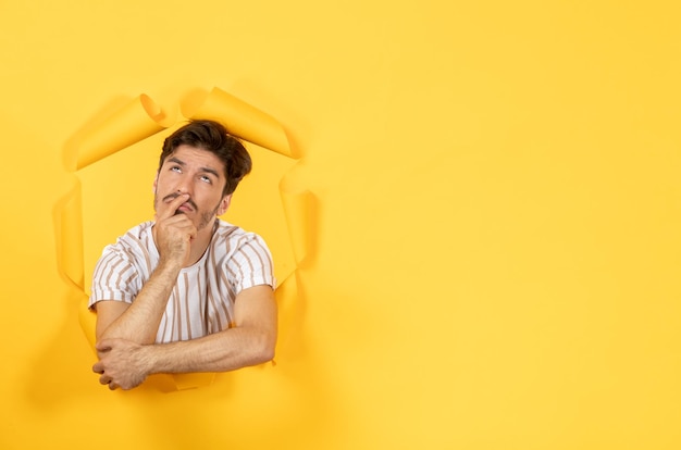 Hombre joven de pie sobre el fondo de papel amarillo rasgado chico facial de venta interior