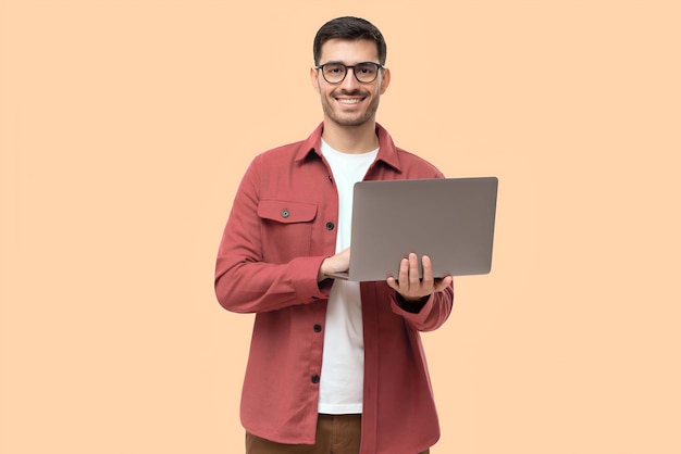 Hombre joven de pie sosteniendo una computadora portátil y mirando a la cámara con una sonrisa feliz