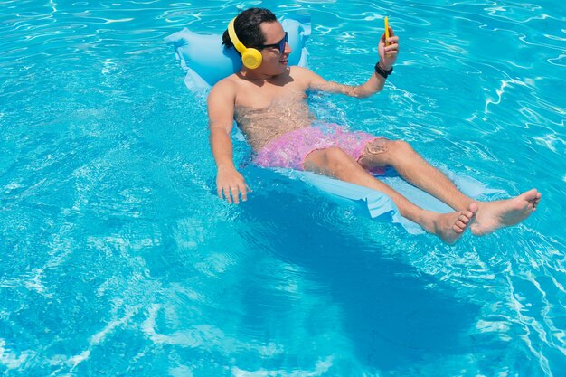 Hombre joven en la piscina con su teléfono celular.