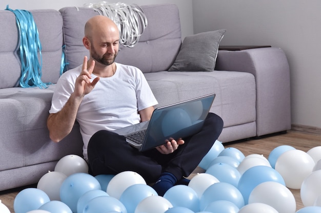 Hombre joven positivo en ropa casual sentado en la sala de estar y usando la computadora portátil