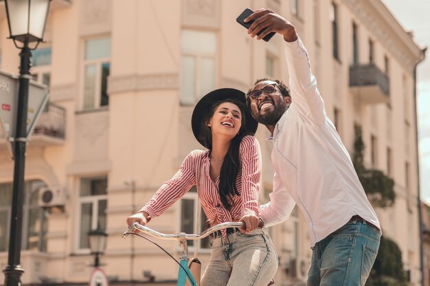 Hombre joven positivo tomando selfie con su novia en la bicicleta