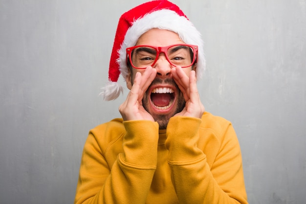 Hombre joven que celebra el día de Navidad con regalos gritando algo feliz al frente