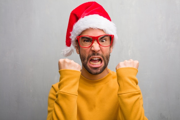 Hombre joven que celebra el día de Navidad con regalos gritando muy enojado y agresivo