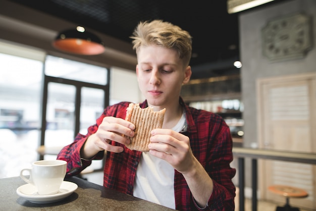 Hombre joven que cena el emparedado de panini en restaurante.