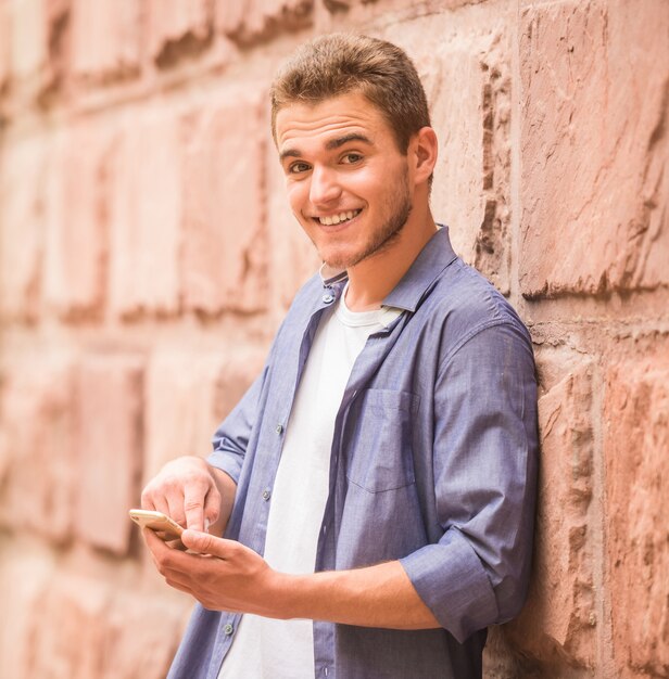 Hombre joven que se coloca con su teléfono cerca de la pared.