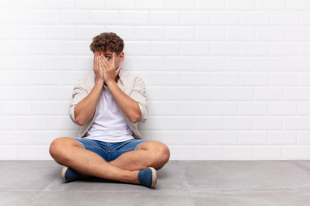 Hombre joven que cubre la cara con las manos, mirando entre los dedos con expresión de sorpresa