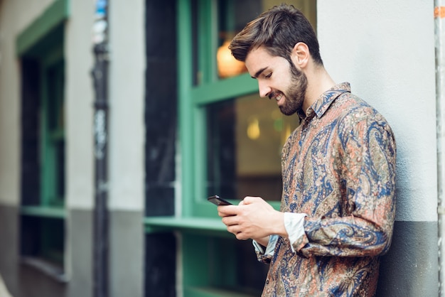 Hombre joven que desgasta la ropa casual que mira su smartphone en la calle.