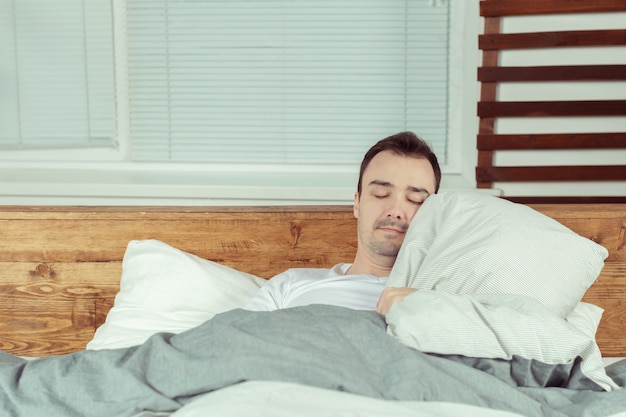 Hombre joven que duerme en cama en dormitorio