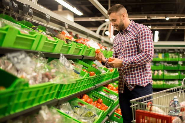 Hombre joven que elige los tomates frescos en supermercado