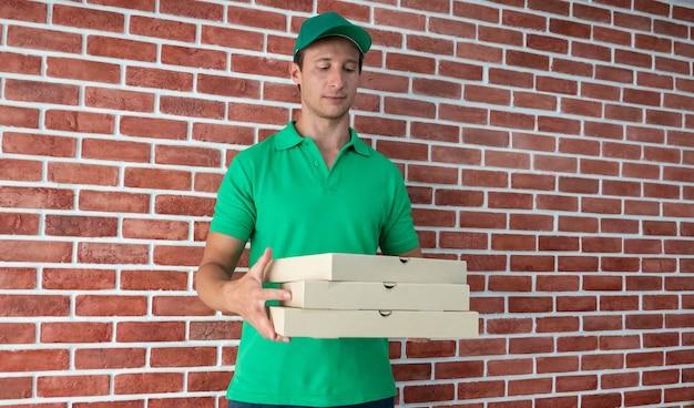 Hombre joven que entrega comida al cliente en la puerta, bolsillo de papel y contenedores de comida en manos de un repartidor sonriente al aire libre. Servicio de calidad de un restaurante.