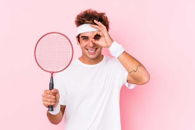 El hombre joven que jugaba a bádminton aisló excitado manteniendo gesto aceptable en ojo.