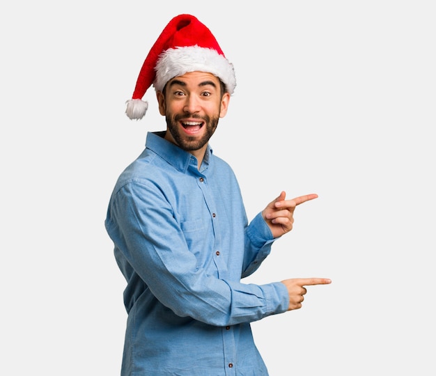 Hombre joven que lleva el sombrero de santa que señala al lado con el dedo