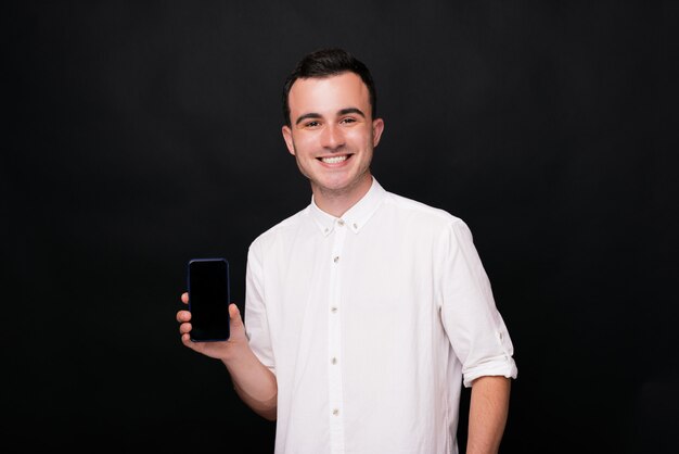 Hombre joven que muestra la pantalla en blanco de su teléfono en el fondo negro que hace publicidad de algo.