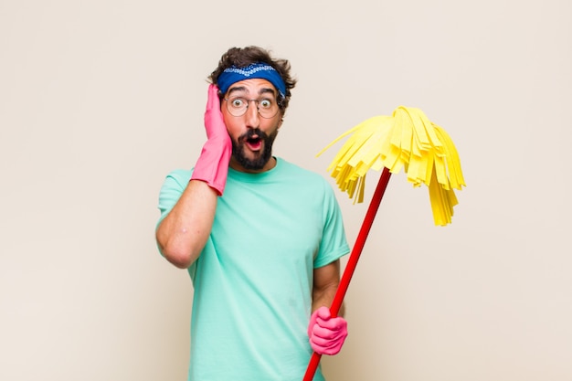 Foto hombre joven que parece emocionado y sorprendido, con la boca abierta con ambas manos en la cabeza, sintiéndose como un afortunado ganador