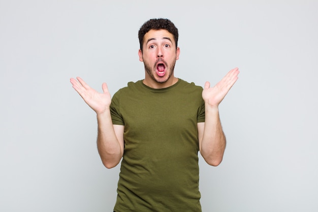 Hombre joven que parece feliz y emocionado, sorprendido con una sorpresa inesperada con ambas manos abiertas junto a la cara