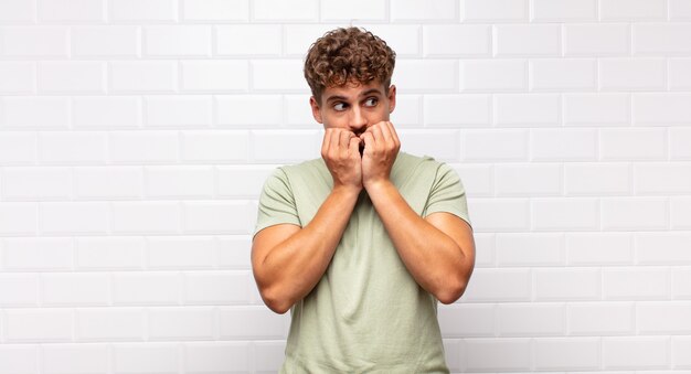 Hombre joven que parece preocupado, ansioso, estresado y asustado, mordiéndose las uñas y mirando al espacio de copia lateral