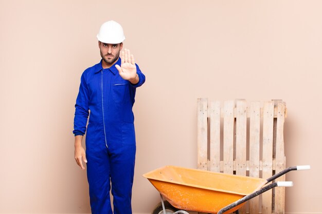 Hombre joven que parece serio, severo, disgustado y enojado mostrando la palma abierta haciendo gesto de parada concepto de construcción