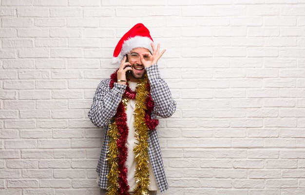 Hombre joven que se sienta con los regalos que celebran la Navidad confidente que hace gesto aceptable en ojo