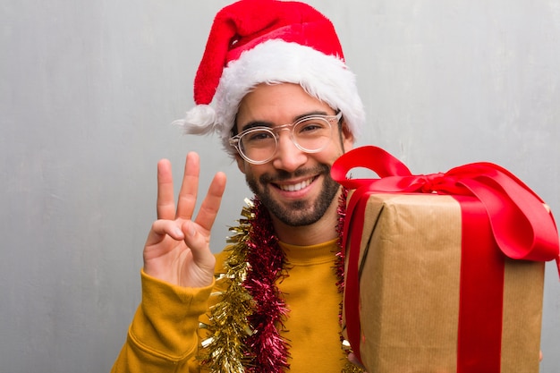 Hombre joven que se sienta con los regalos que celebran la Navidad que muestra el número tres