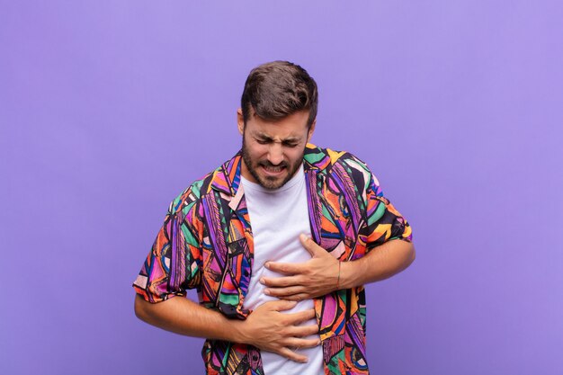 Hombre joven que se siente ansioso, enfermo, enfermo e infeliz, que sufre dolor de estómago o gripe