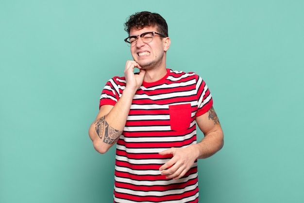 Hombre joven que se siente estresado, frustrado y cansado, frotando el cuello doloroso, con una mirada preocupada y preocupada