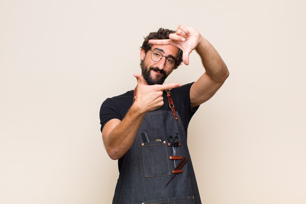 Hombre joven que se siente feliz, amigable y positivo, sonriendo y haciendo un retrato o marco de fotos con las manos