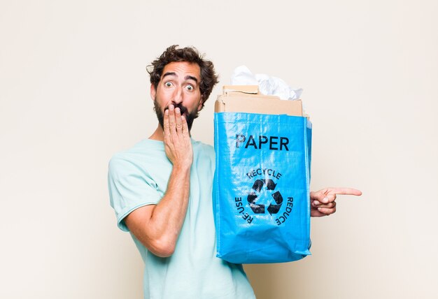 Hombre joven que se siente feliz, conmocionado y sorprendido, cubriendo la boca con la mano y apuntando al espacio de copia lateral