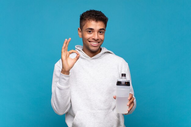 Hombre joven que se siente feliz, relajado y satisfecho, mostrando aprobación con gesto bien, sonriendo. concepto de deporte