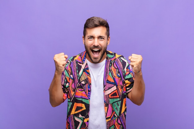 Hombre joven que se siente feliz, sorprendido y orgulloso, gritando y celebrando el éxito con una gran sonrisa