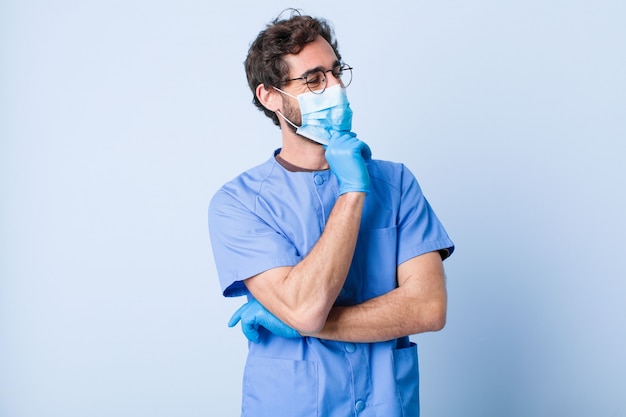 Hombre joven que sonríe con una expresión feliz, confiada con la mano en la barbilla, preguntándose y mirando a un lado. concepto de coronavirus