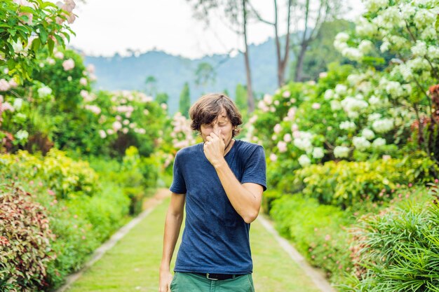 Hombre joven que sopla la nariz frente a un árbol floreciente Concepto de alergia primaveral