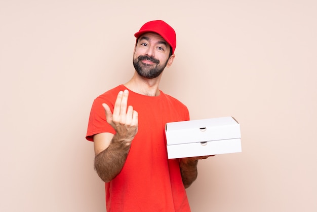 Hombre joven que sostiene una pizza sobre fondo aislado que invita a venir con la mano. Feliz de que hayas venido