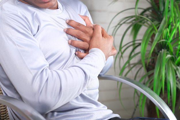 Foto hombre joven que sufre de dolor en el corazón y que sostiene el pecho con la mano.