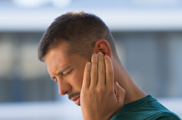 Hombre joven que sufre de dolor de oído otitis tinnitus o inflamación del oído