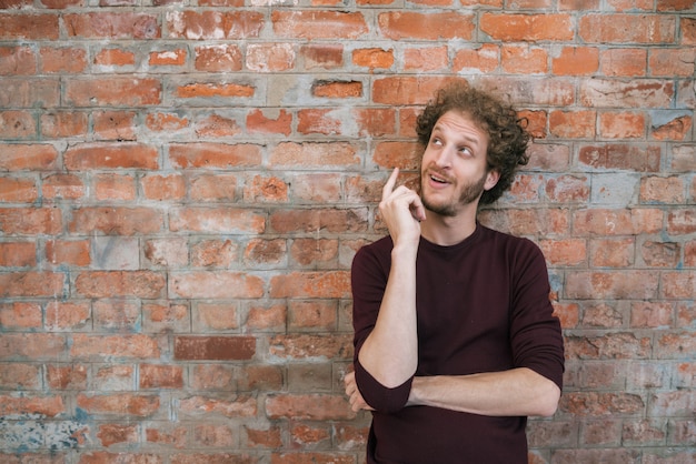 Hombre joven que tiene una idea contra la pared de ladrillo.