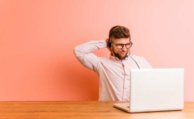 Hombre joven que trabaja en un call center que sufre dolor de cuello debido al estilo de vida sedentario.