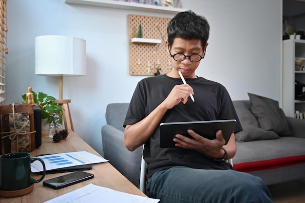 Hombre joven que trabaja con tableta digital en casa.