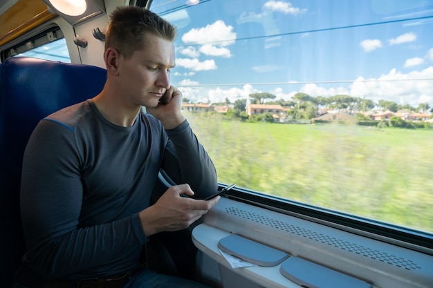 Hombre joven que viaja en tren mediante teléfono móvil.