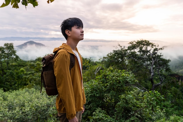 Hombre joven que va de viaje por la naturaleza con mochila detrás es mar de niebla y montañas. admirando la naturaleza, relajándose.