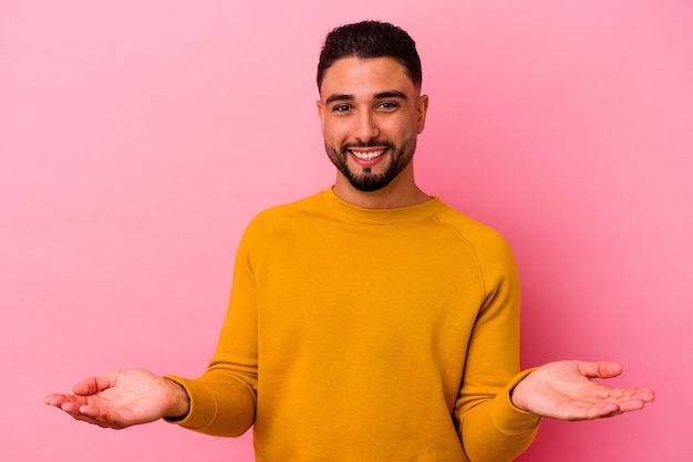 Hombre joven de raza mixta aislado en rosa mostrando una expresión de bienvenida.